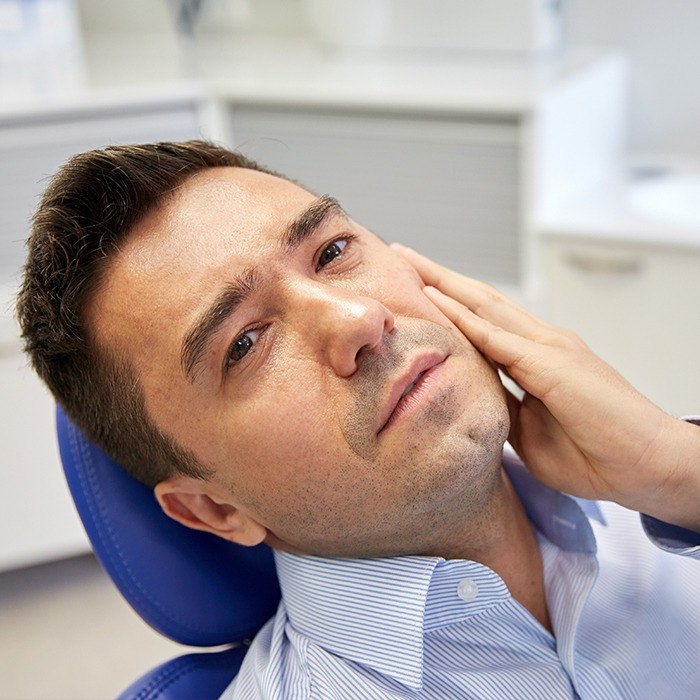Man holding cheek in dental chair