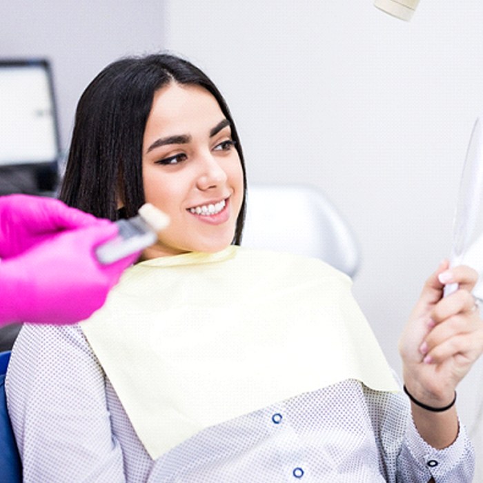 A young female looking at her repaired smile in the mirror at the dentist’s office