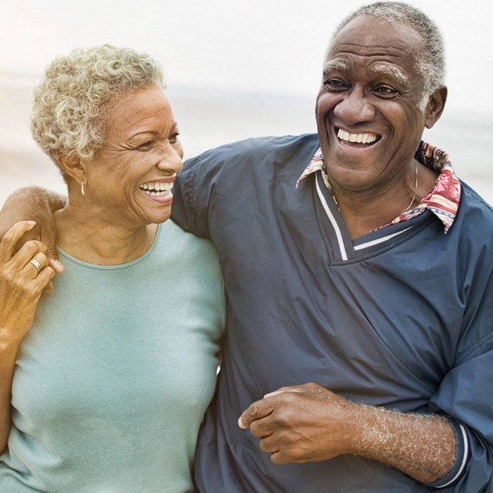 An older couple walking along the beach and smiling after receiving their dental implants