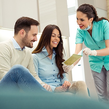 Smiling couple reviewing pamphlet with dental assistant