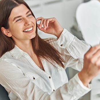 Woman smiling at reflection in handheld mirror