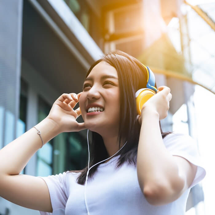 person smiling and walking down a street with headphones on