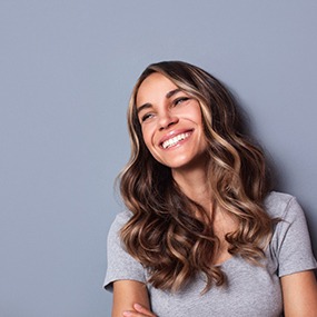 Woman in grey shirt leaning on wall and smiling