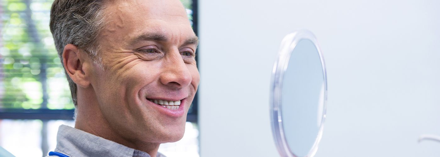 Man in dental chair looking at smile in mirror