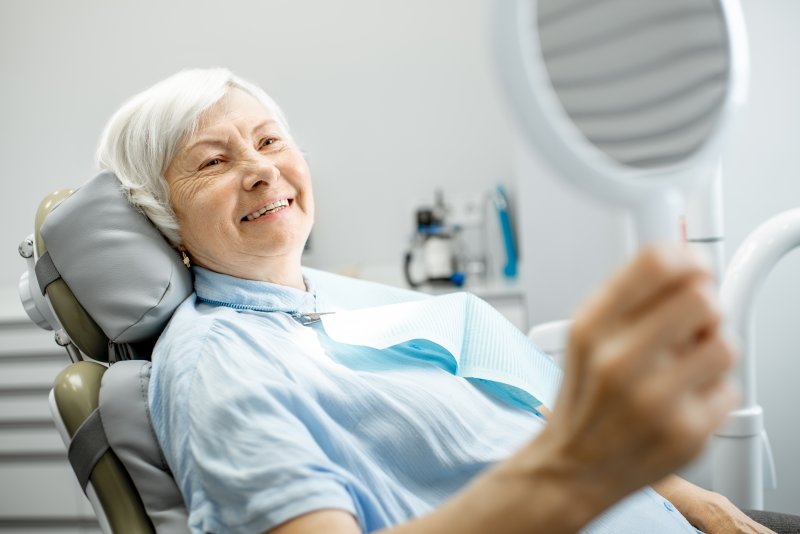 Elderly patient smiling in mirror at appointment