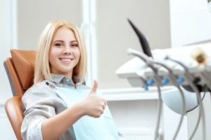 Woman in dental chair with blonde hair smiling with thumb up 