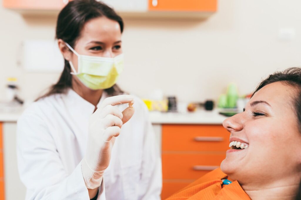 Dentist in yellow mask showing patient her extracted tooth